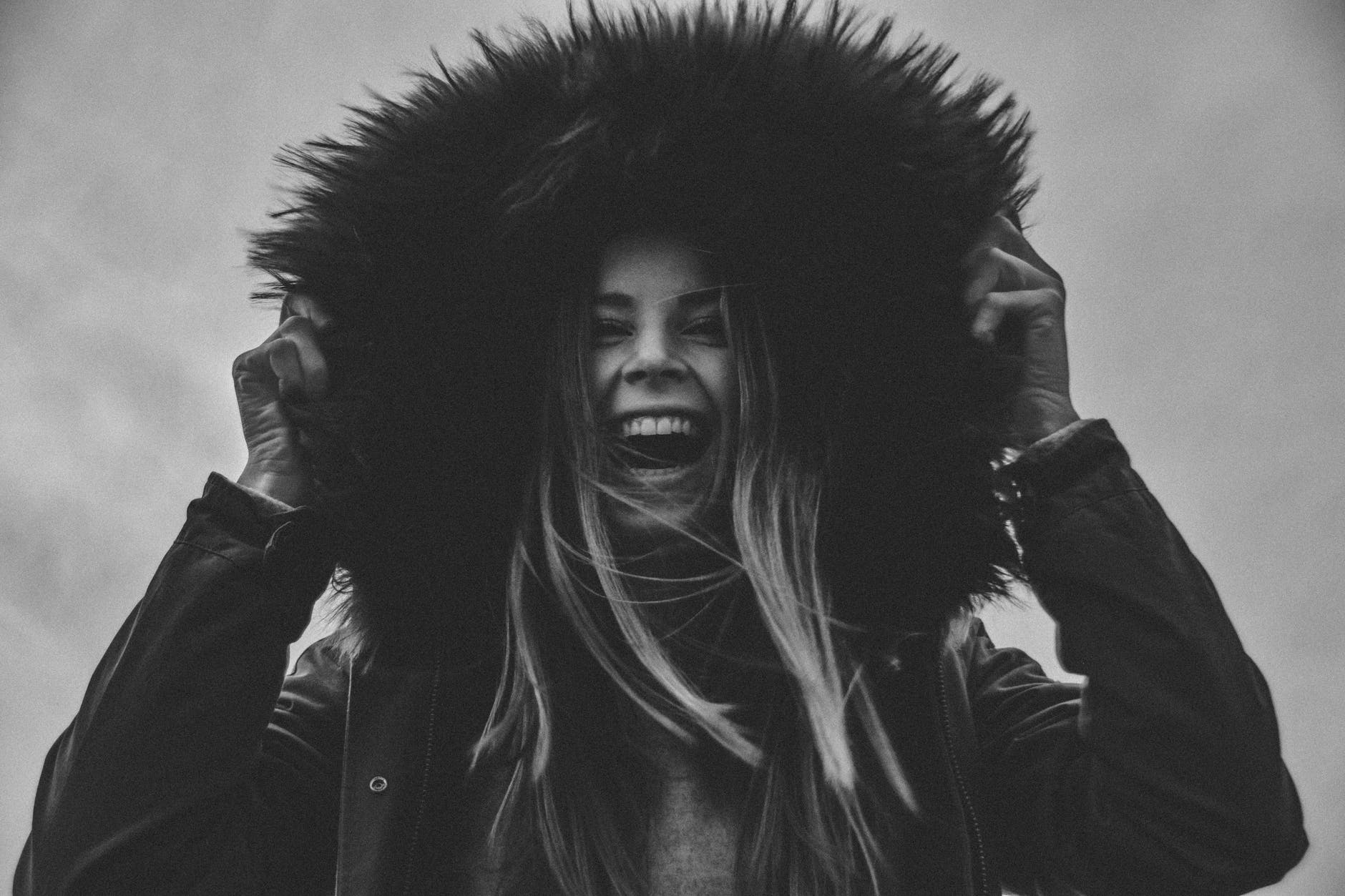 grayscale photo of laughing woman holding her hat