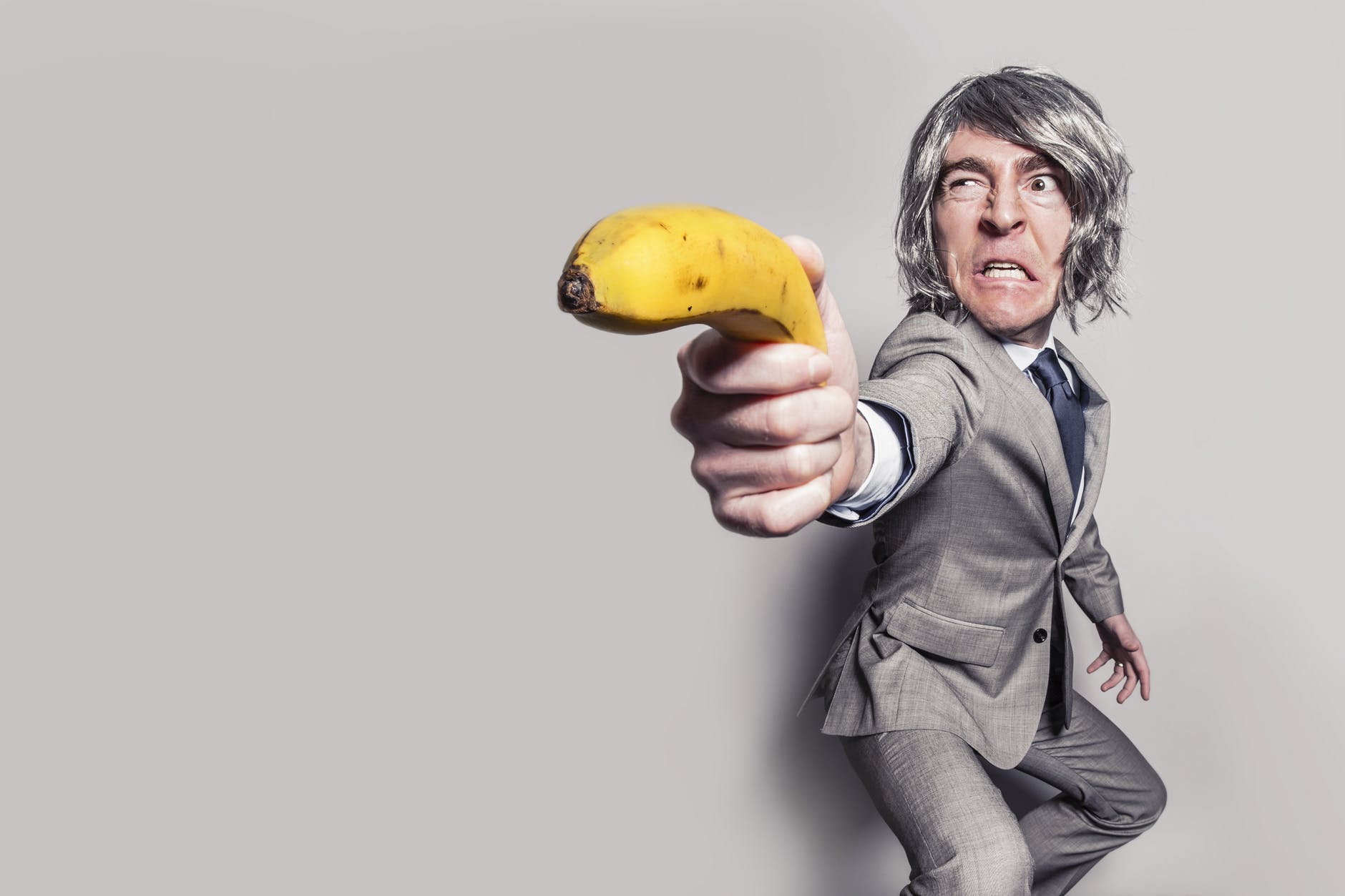 man in gray suit jacket holding yellow banana fruit while making face