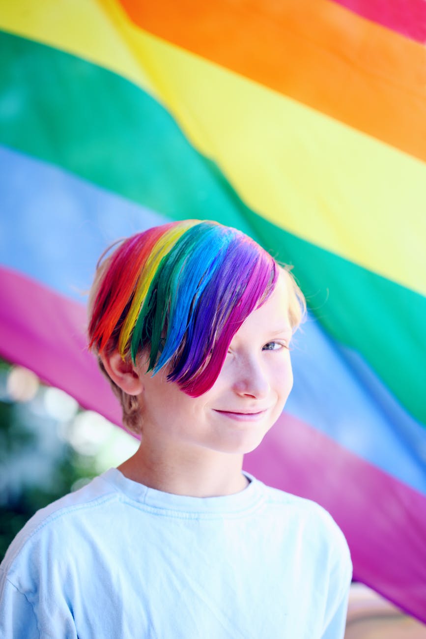boy wearing white shirt with iridescent hair color infront of flag