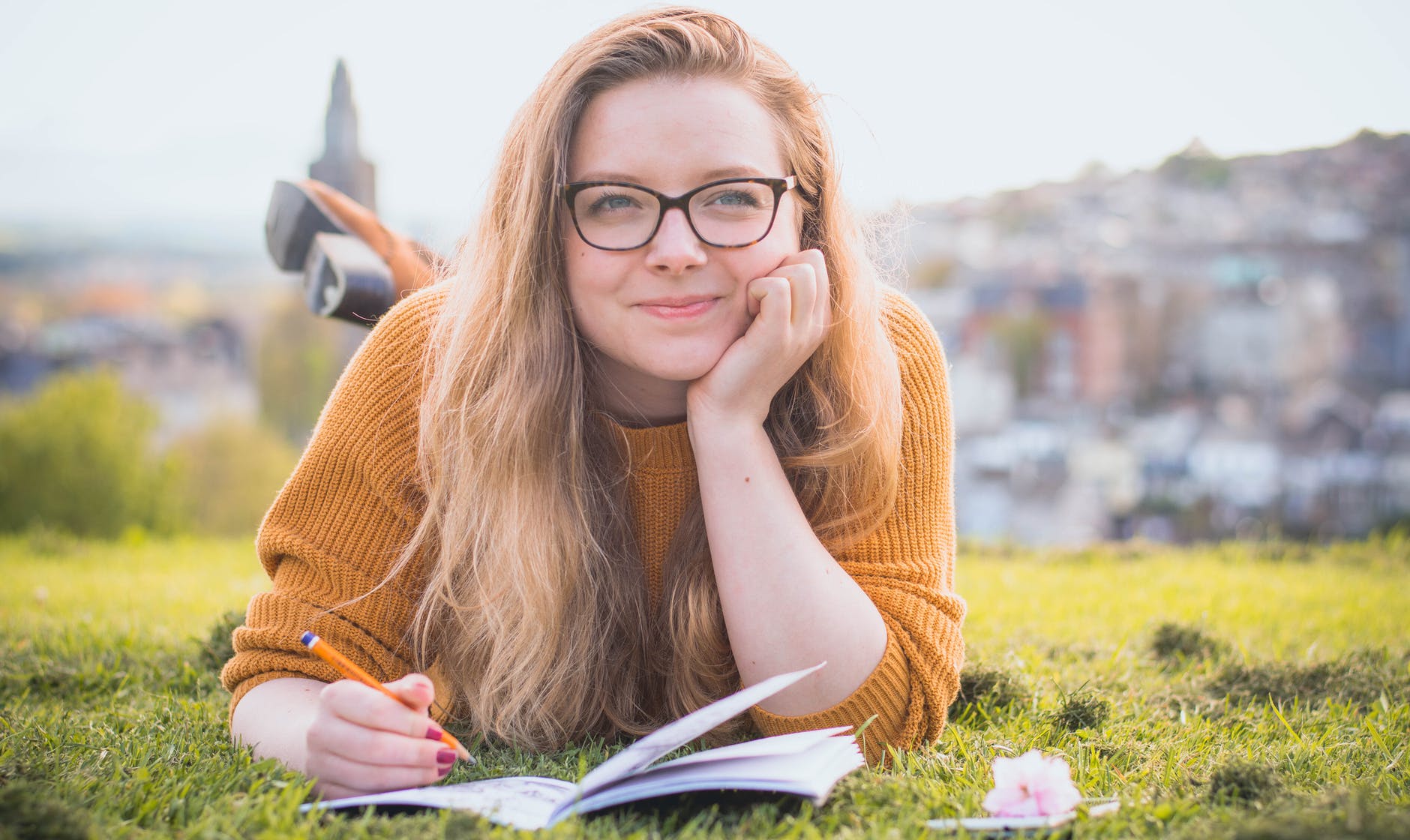 woman lying on green grass while holding pencil