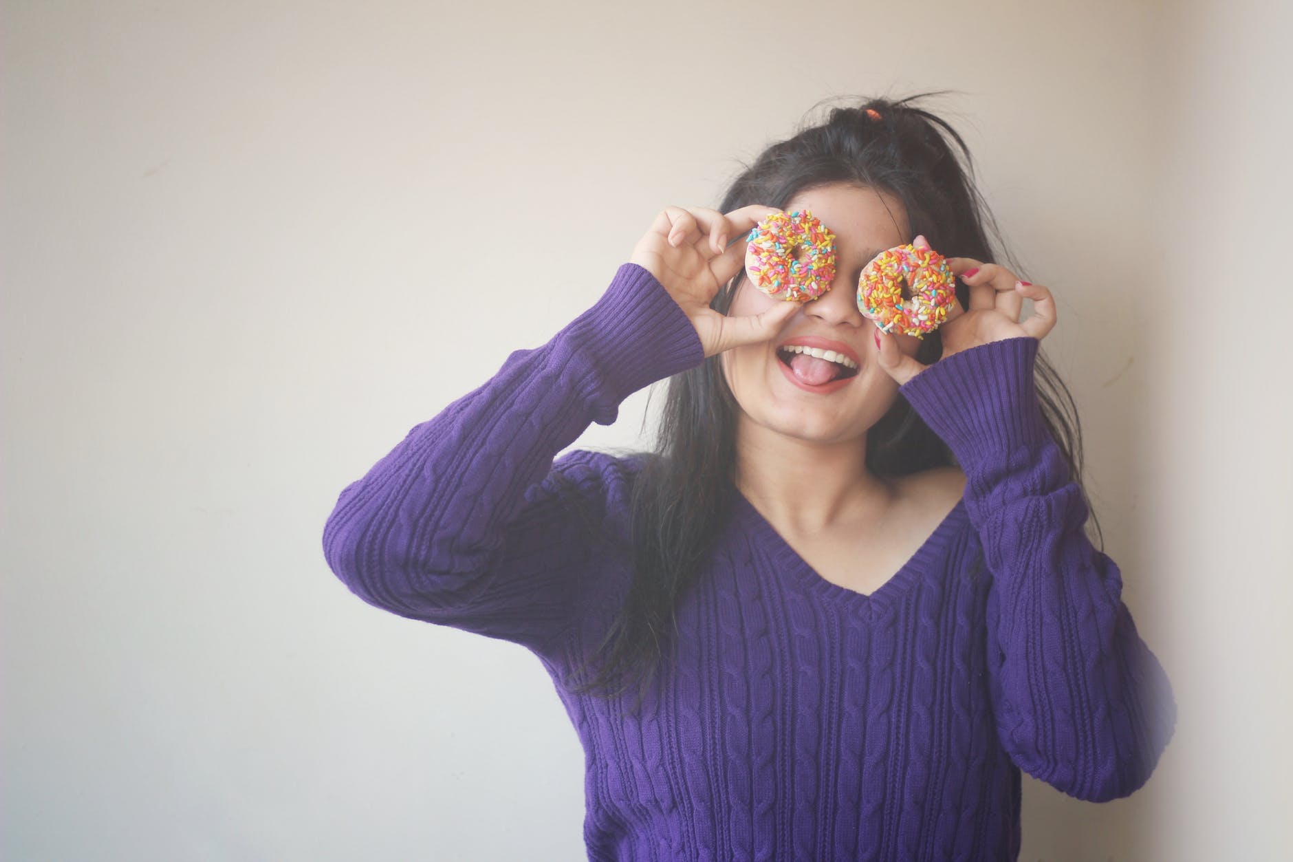 woman wearing sweater covering her eyes with doughnuts
