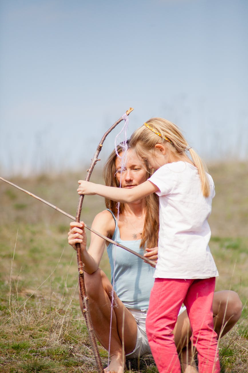 photo of woman teaching her child on how to use bow and arrow
