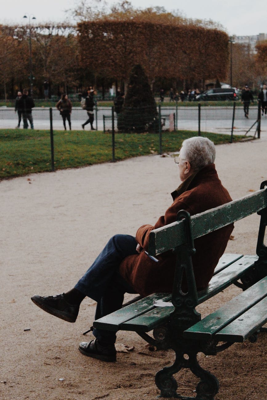 elderly man sitting on bench in park during autumn day