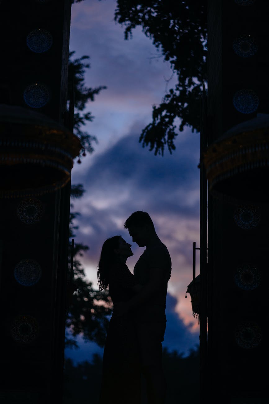 silhouettes of hugging couple standing in arch in darkness